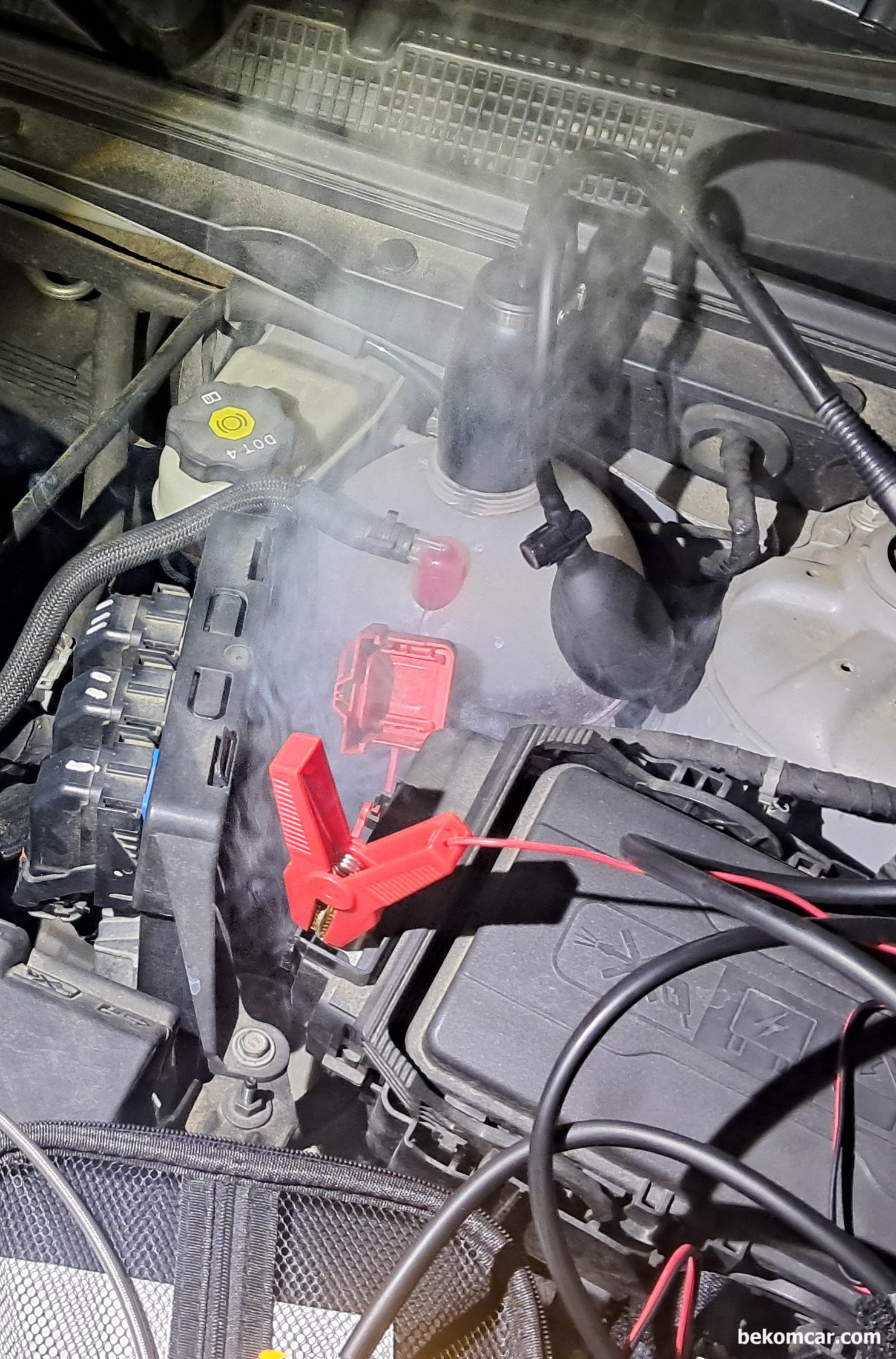 쉐보레 말리부 1.5T 실린더내시경 및 헤드가스켓 냉각수리크 진단과정 기록, 헤드 개스킷 누스 점검을 위하여 스모크 머신 세팅을 하고 있다. 냉각수 보조 통에 연기와 압력을 주고, 엔진 헤드와 블록 사이에서 냉각수가 흘러나오는지 확인하는 과정이다. 그런데 예상 못 한 변수가 발생, 냉각수 보조 통 아래쪽에서 상당한 연기가 나오고 있다. 자세히 보니 물방울이 보이고 냉각수가 아주 조금씩 새어 나오고 있다. 헤드 개스킷 누수 측정 차량은 쉐보레 말리부 1.5T 에코텍 엔진이다.|bekomcar.com